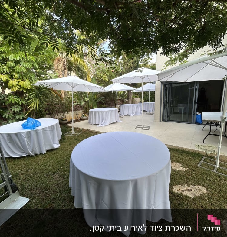שולחנות עגולים עם מפות לבנות בגינה עם שמשיות לבנות